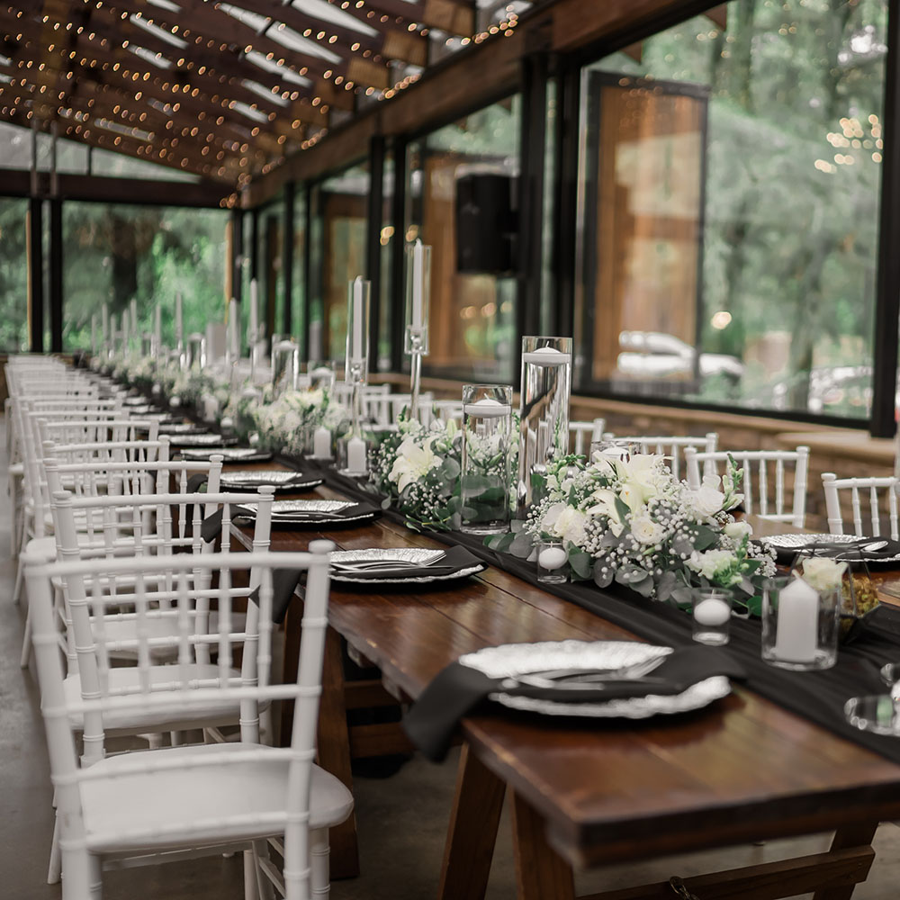 Long timber reception table set with white flowers, candles, black linen and white chairs