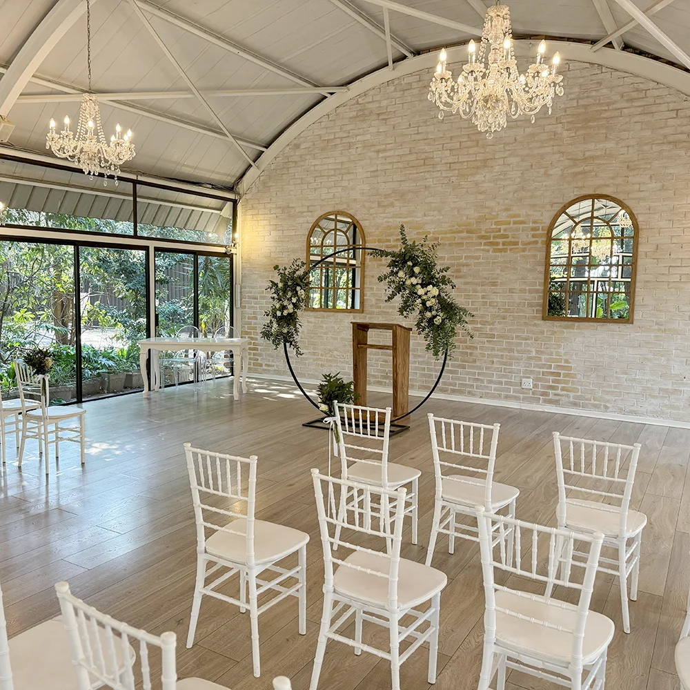 Side view across white ceremony chairs toward the chapel altar and garden-facing glass doors