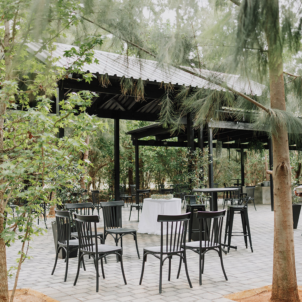 Open-sided black pavilion with tables and chairs beneath mature garden trees